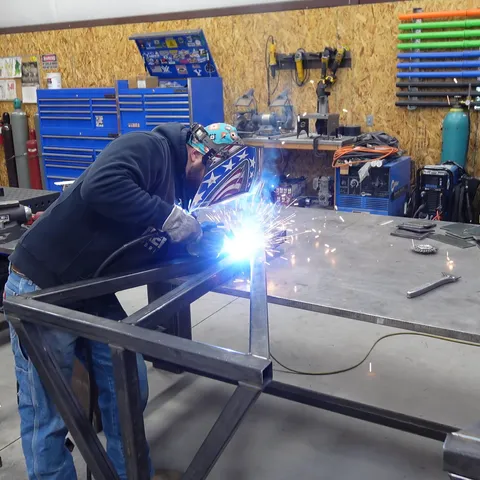 Welder working in shop with American flag backdrop